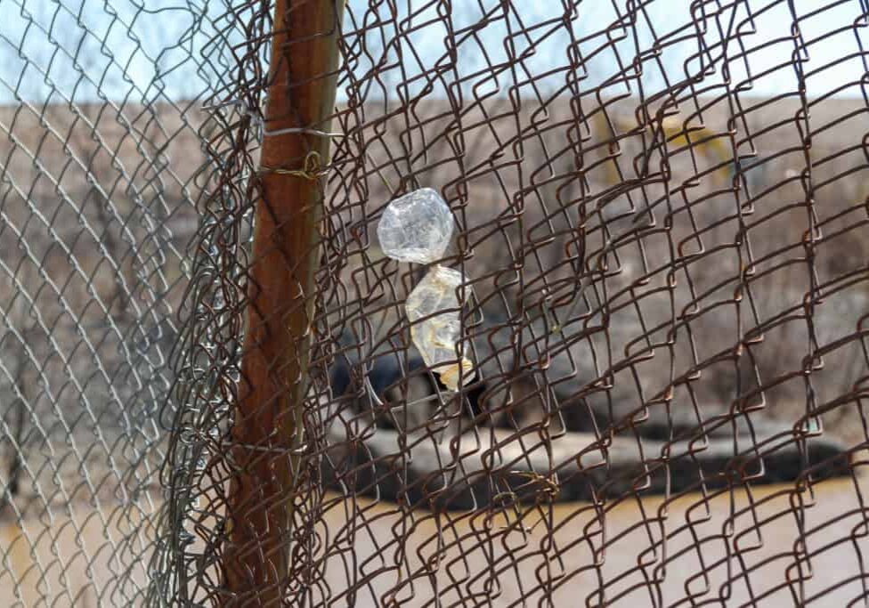 A plastic water bottle stuck in a chain link fence.