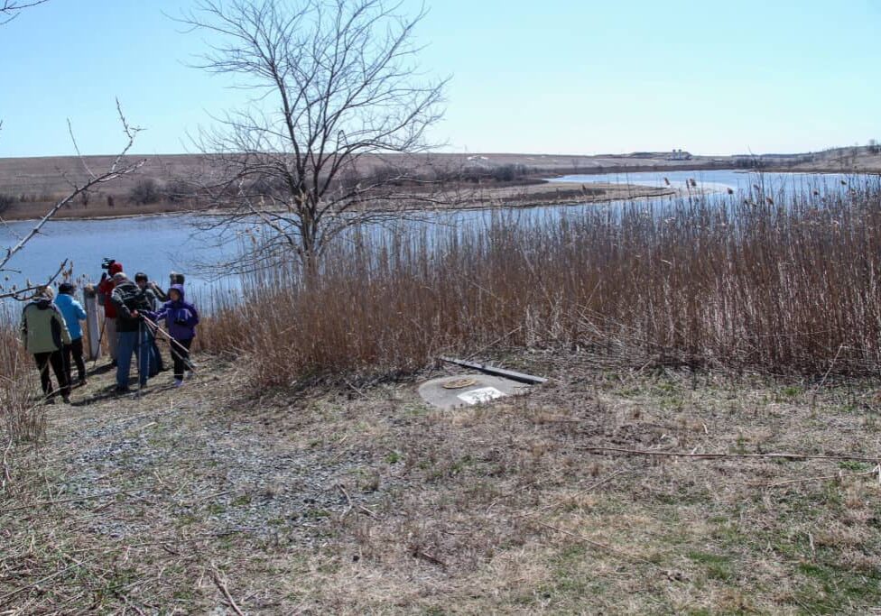 A small group of birdwatchers gathers near a waterway that flows between the mounds at Freshkills Park.